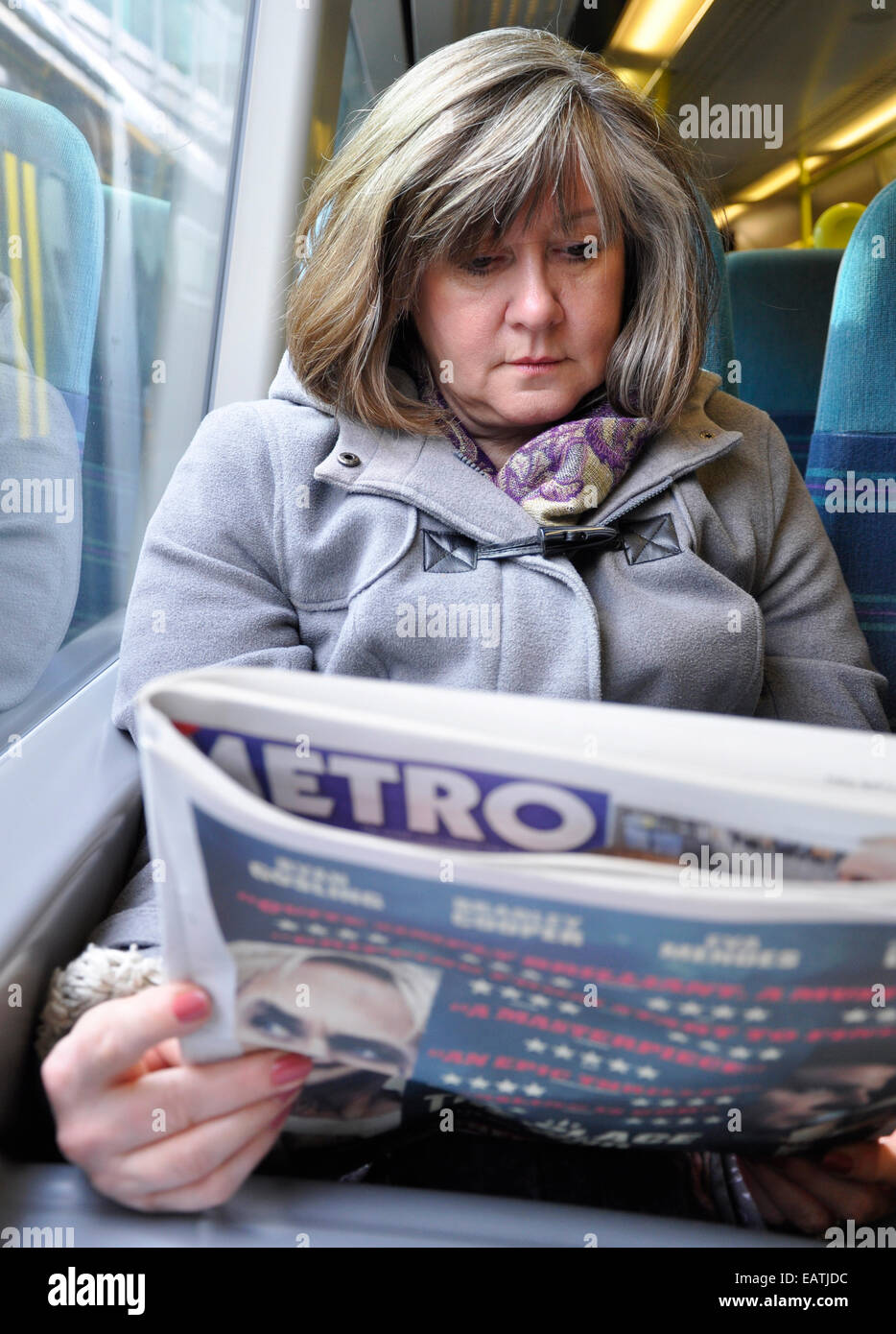 Close-up of smart attractive middle aged woman, reading metro newspaper on London commuter train, London City, England Stock Photo