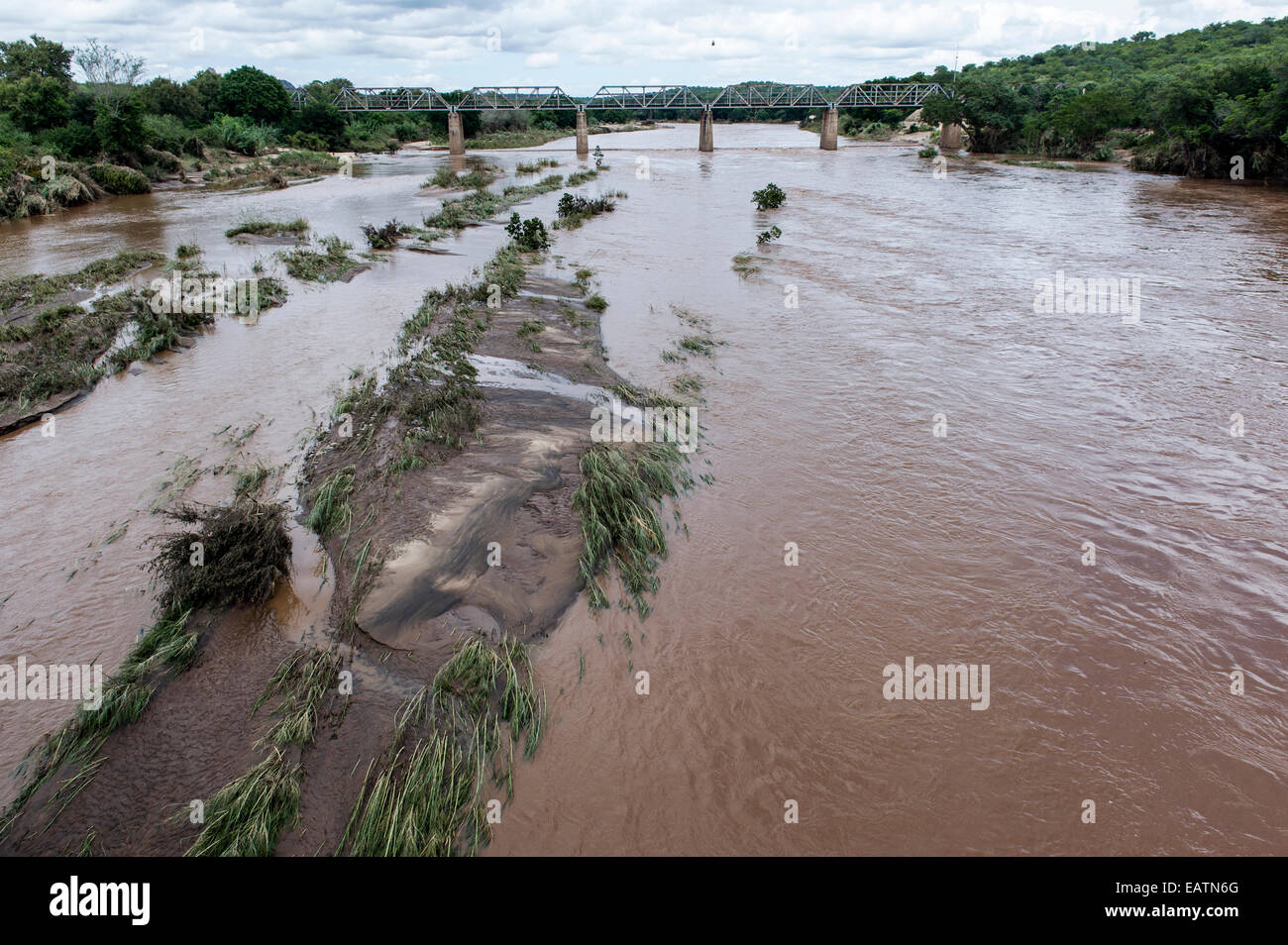 A flooded river swollen with silt flows beneath a railway bridge. Stock Photo