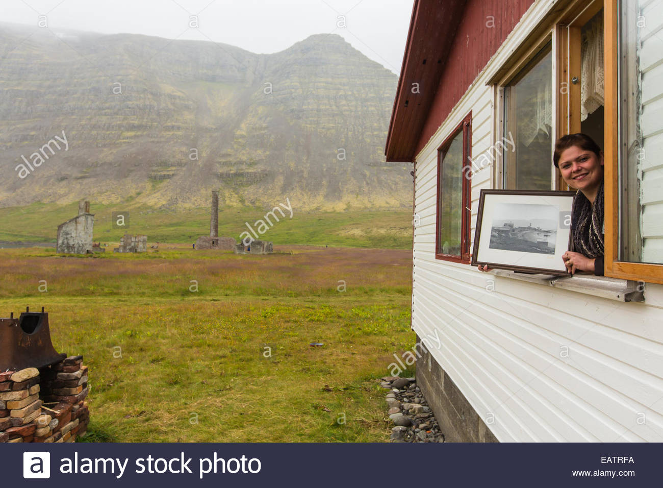 A woman holds a black and white photo of an old whaling station. Stock Photo