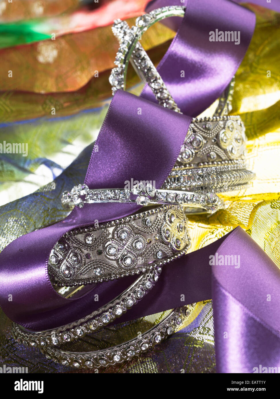 silver ornate bangle bracelets stacked with a decorative purple ribbon on a yellow green background Stock Photo