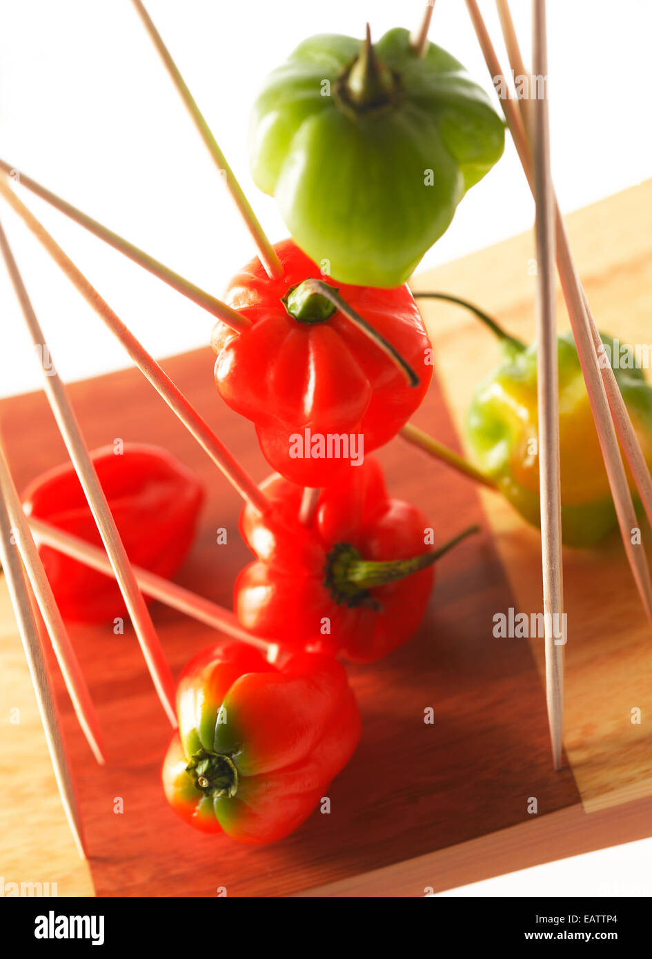 Assorted Habanero peppers on wood skewers on a bamboo cutting board with white background Stock Photo