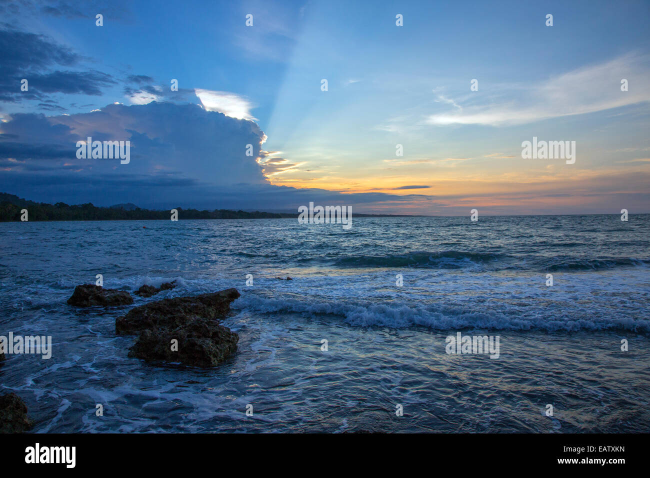 Sunset sunbeams in the evening sky and gentle waves lapping coral rock. Stock Photo