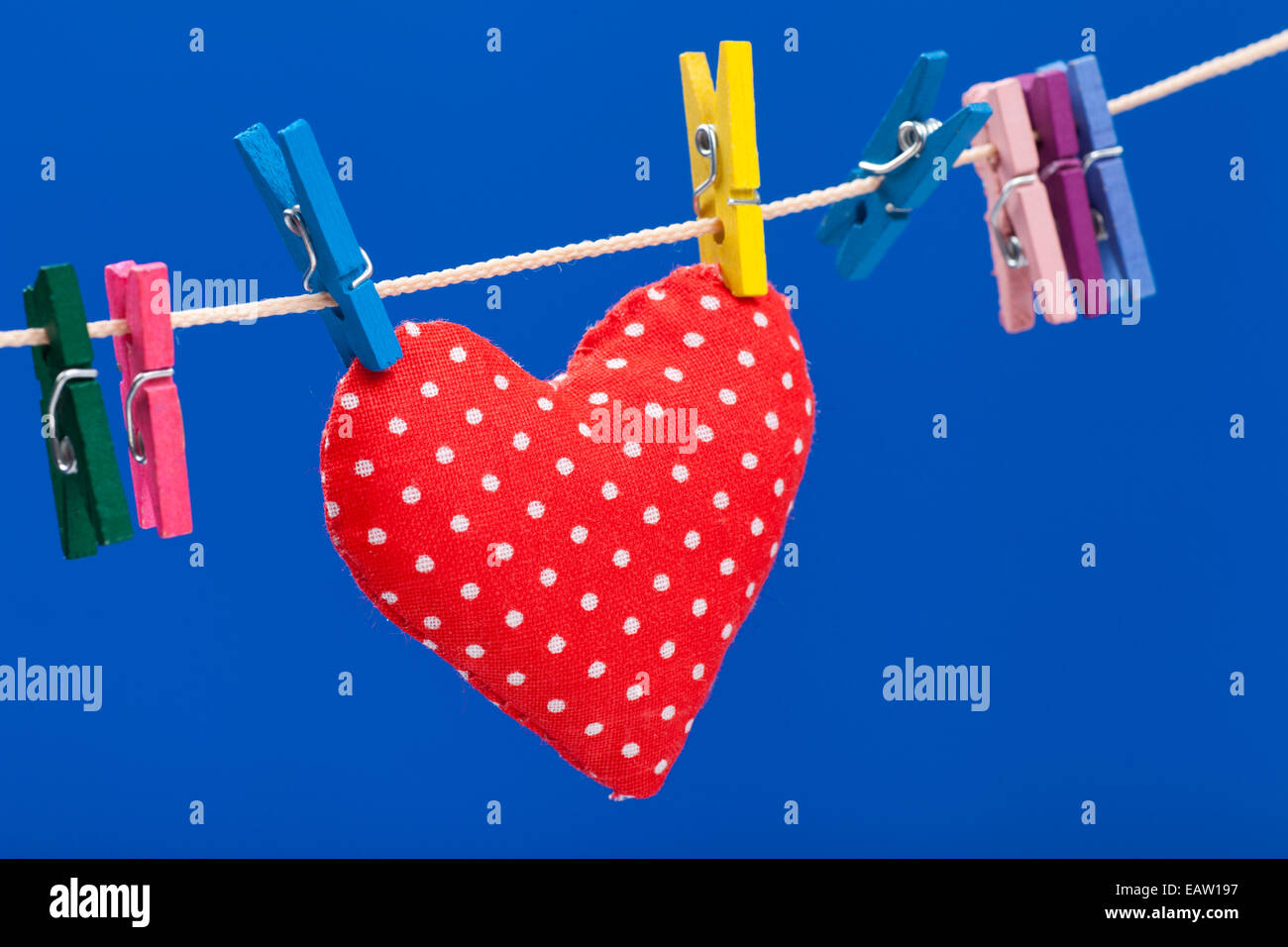 red heart hanging on a clothesline with clothespins, blue background Stock Photo