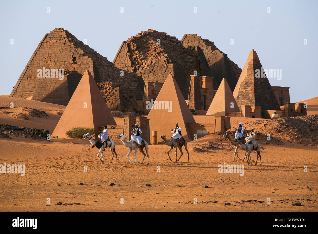 Unidentified Sudanese bedouins ride camels with the famous Meroe pyramids of the ancient Nubian city in the background Stock Photo