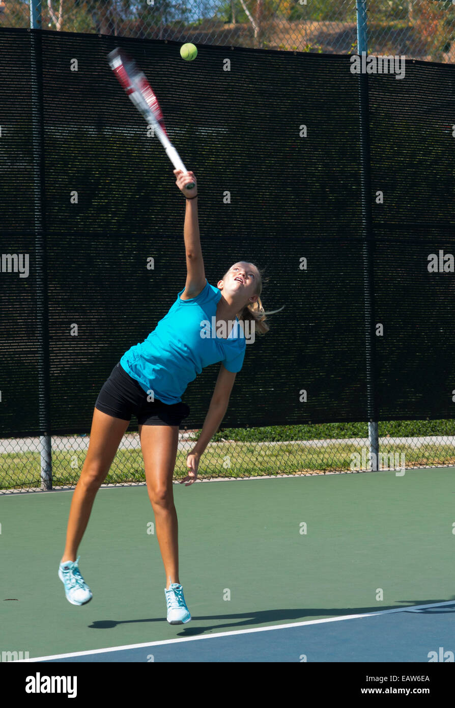 Junior competitive girl's tennis player displaying excellent service technique.  Motion blur. Stock Photo