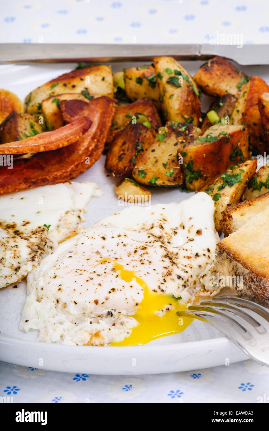 Indulgent breakfast of bacon, potato hashbrown, sunny side eggs, and sourdough toast. Stock Photo