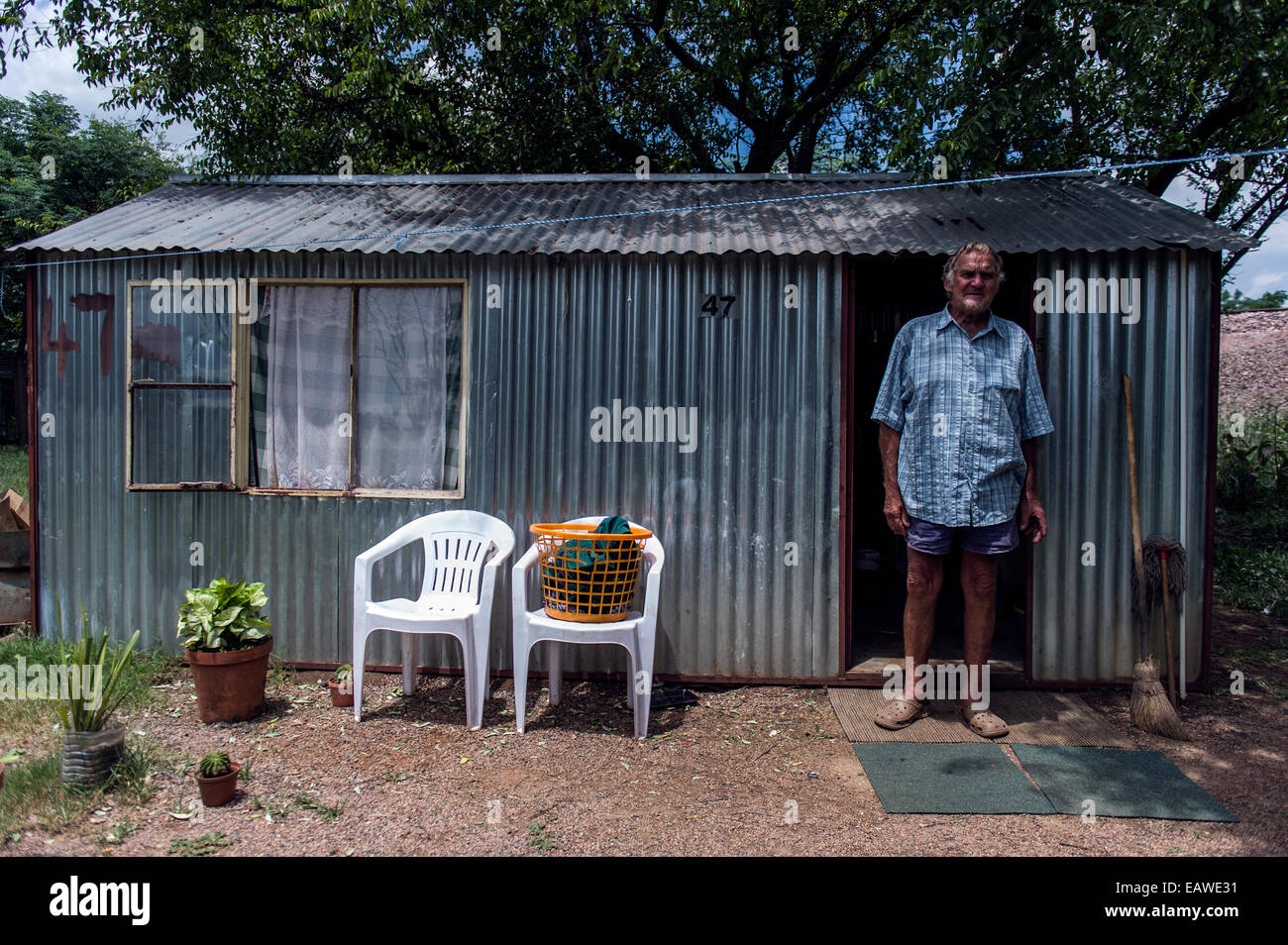 A man stands outside a corrugated tin garden shed that is his home. Stock Photo