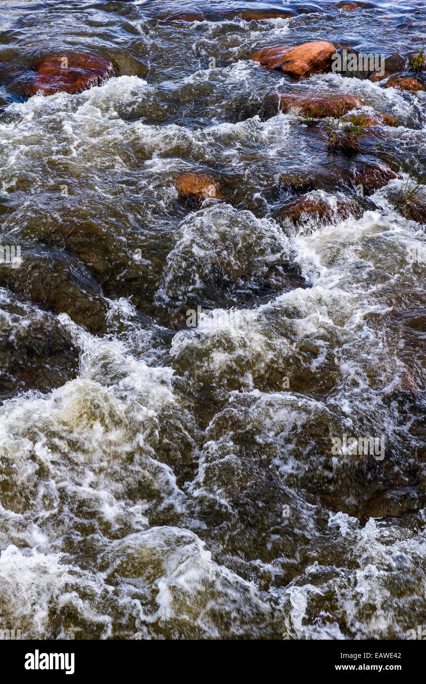 Water cascades and foams as it flows over boulders in a small river. Stock Photo