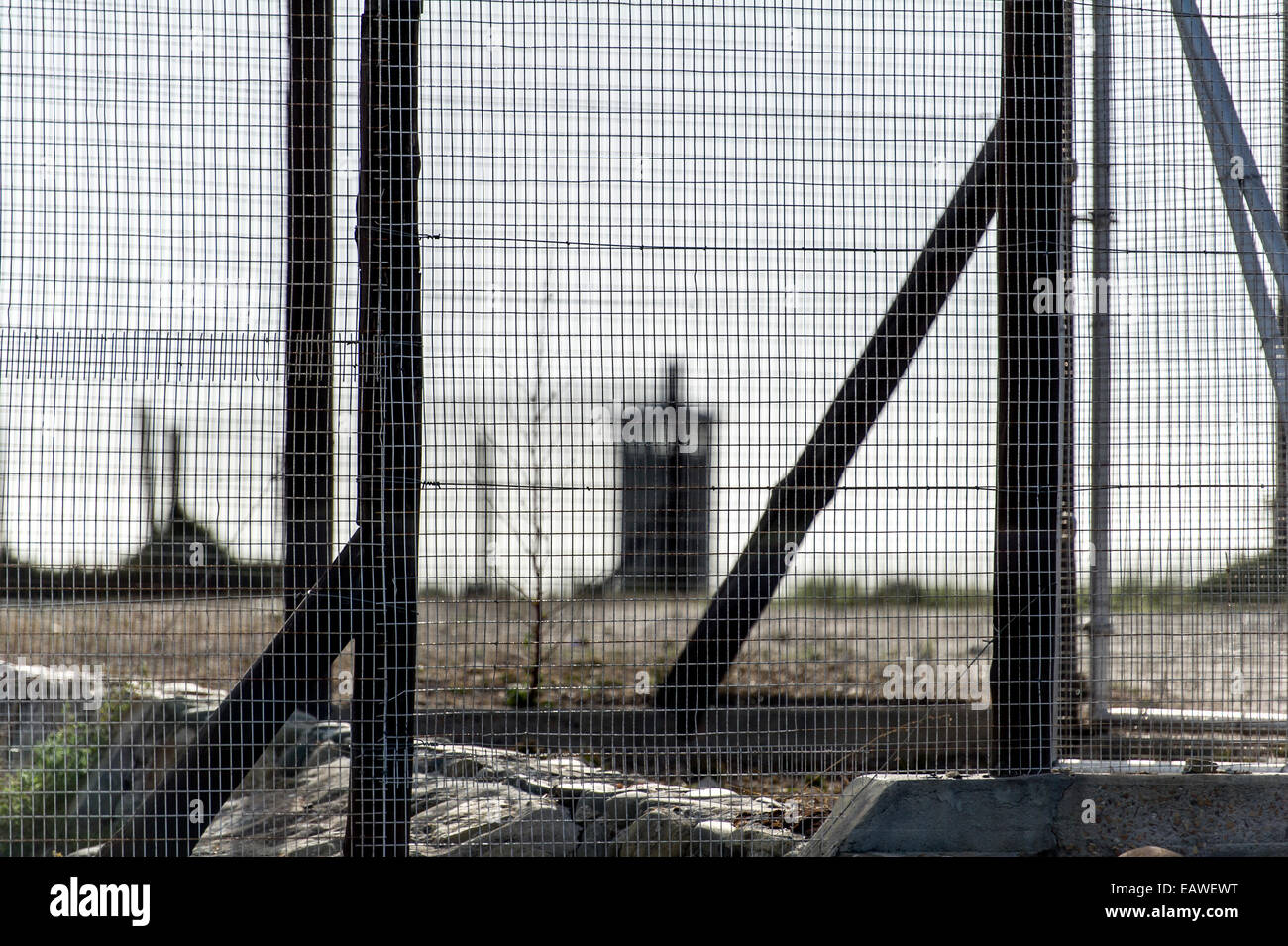 Rows of steel and wire mesh fencing surround a prison and guard tower. Stock Photo