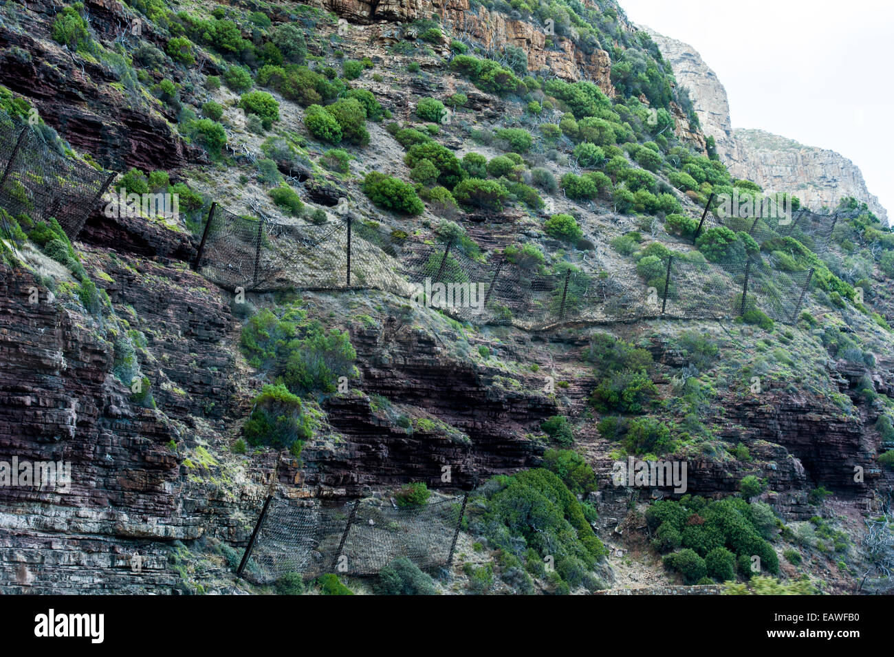 Wire mesh netting catches boulders that fall from a cliff onto a road. Stock Photo