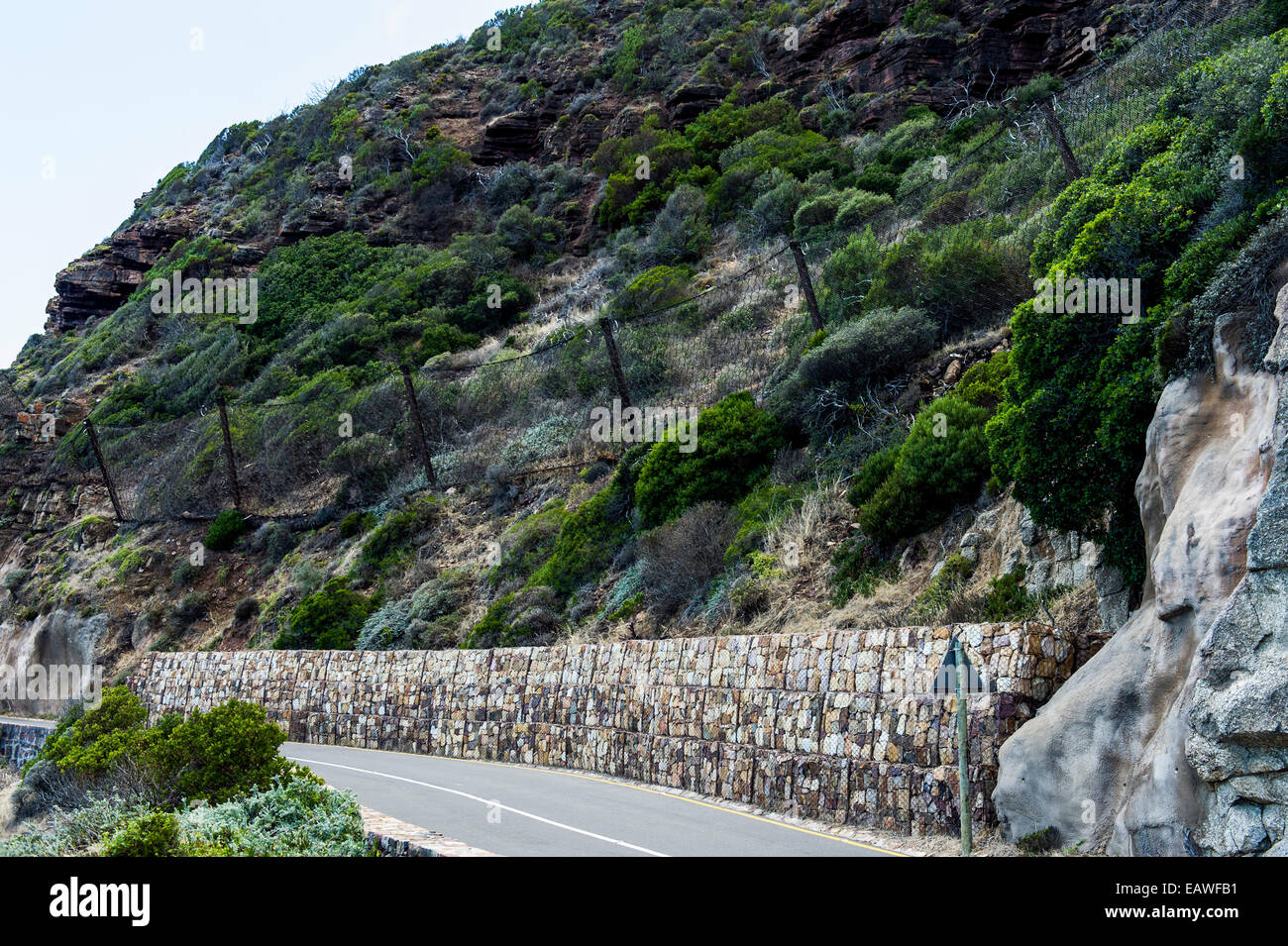 Wire mesh netting catches boulders that fall from a cliff onto a road. Stock Photo