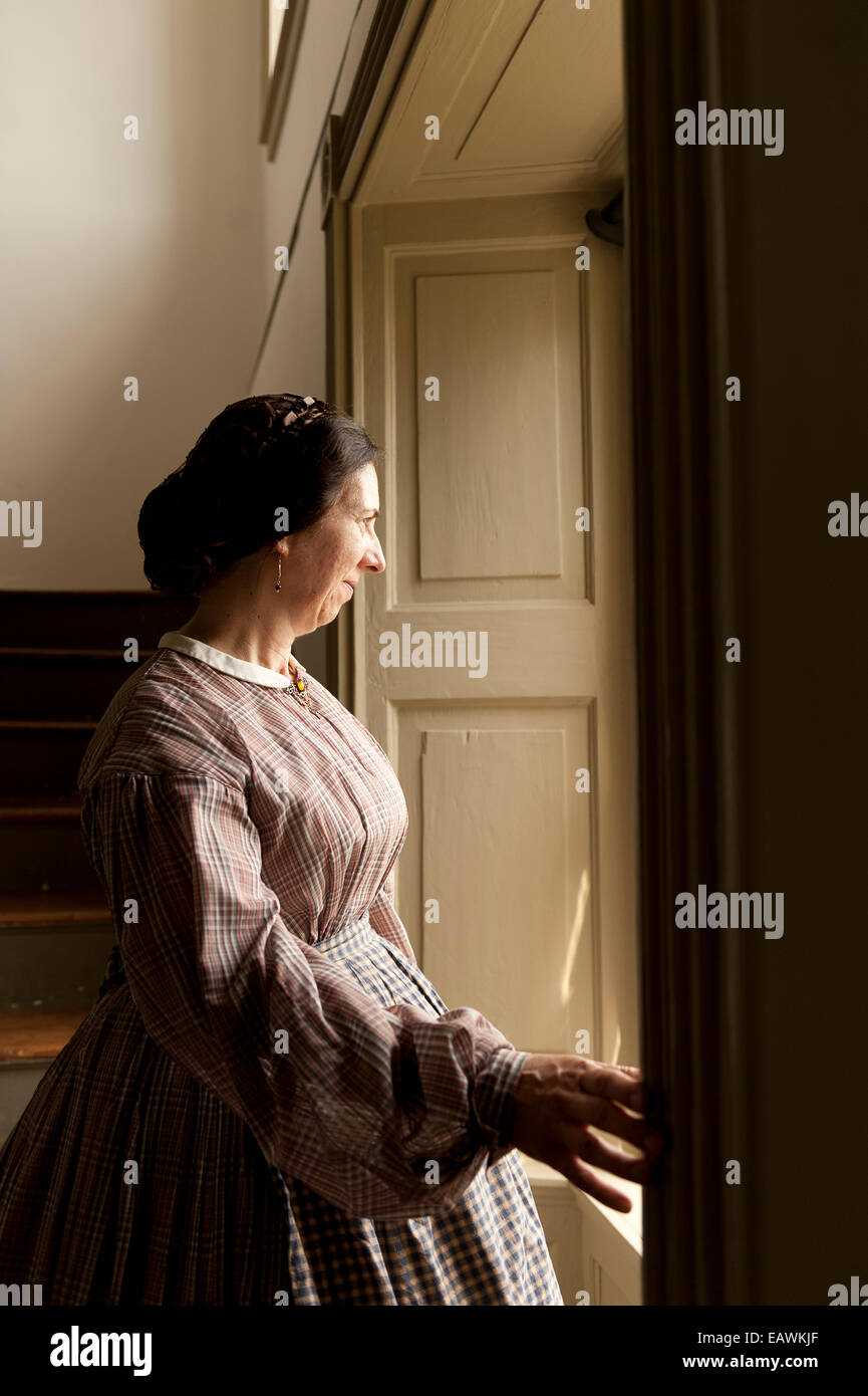 A woman in Civil War era costume stands by a window. Stock Photo