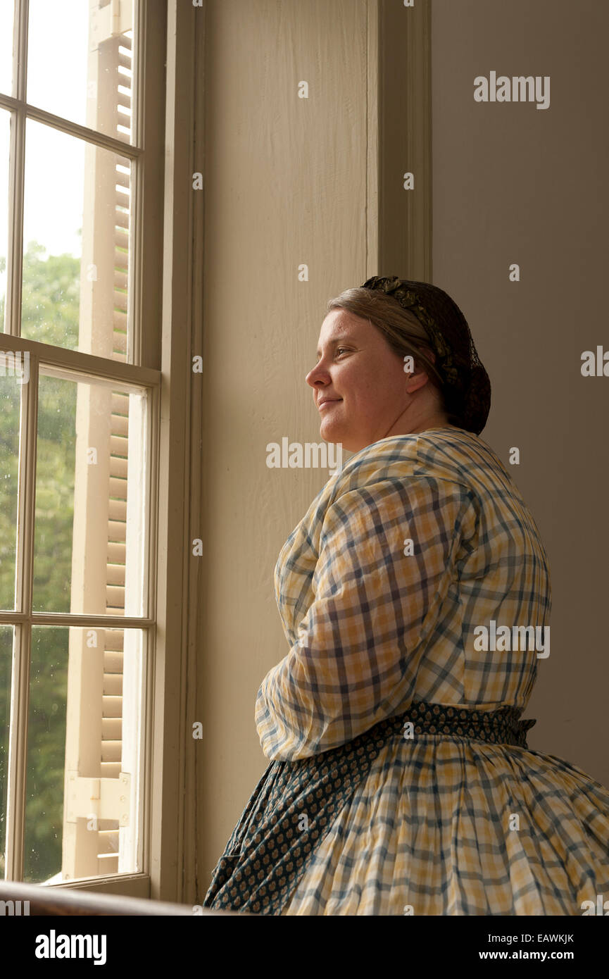 A woman in Civil War era costume stands by a window. Stock Photo