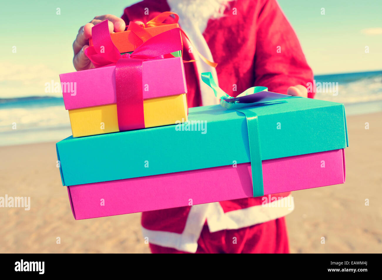 santa claus carrying a pile of gifts on the beach Stock Photo