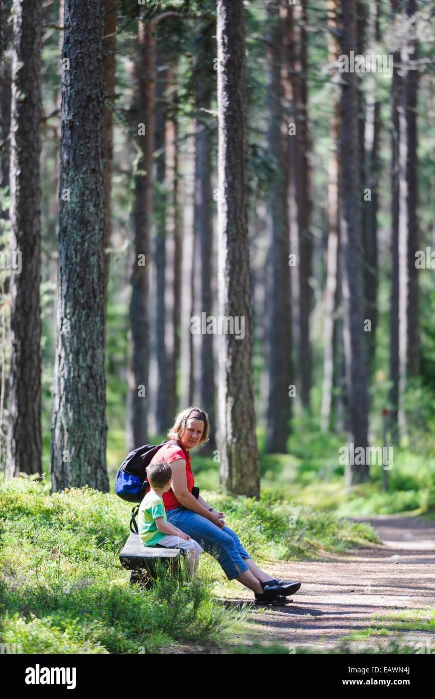 Mother and young son sit on a bench in the woods Stock Photo