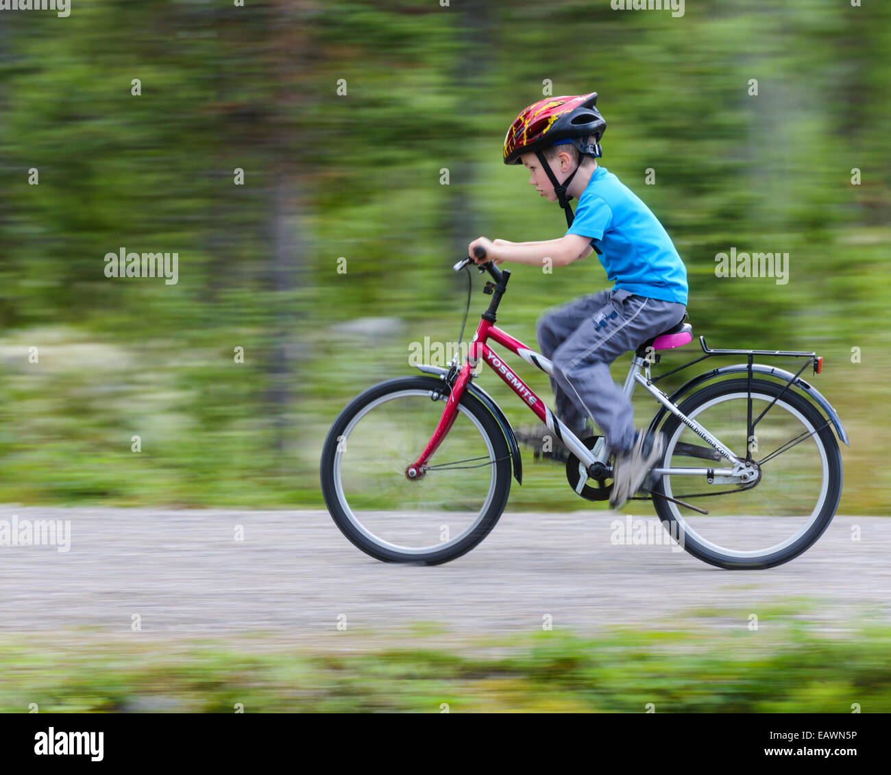 Young boy rides his bicycle down a paved forest path Stock Photo