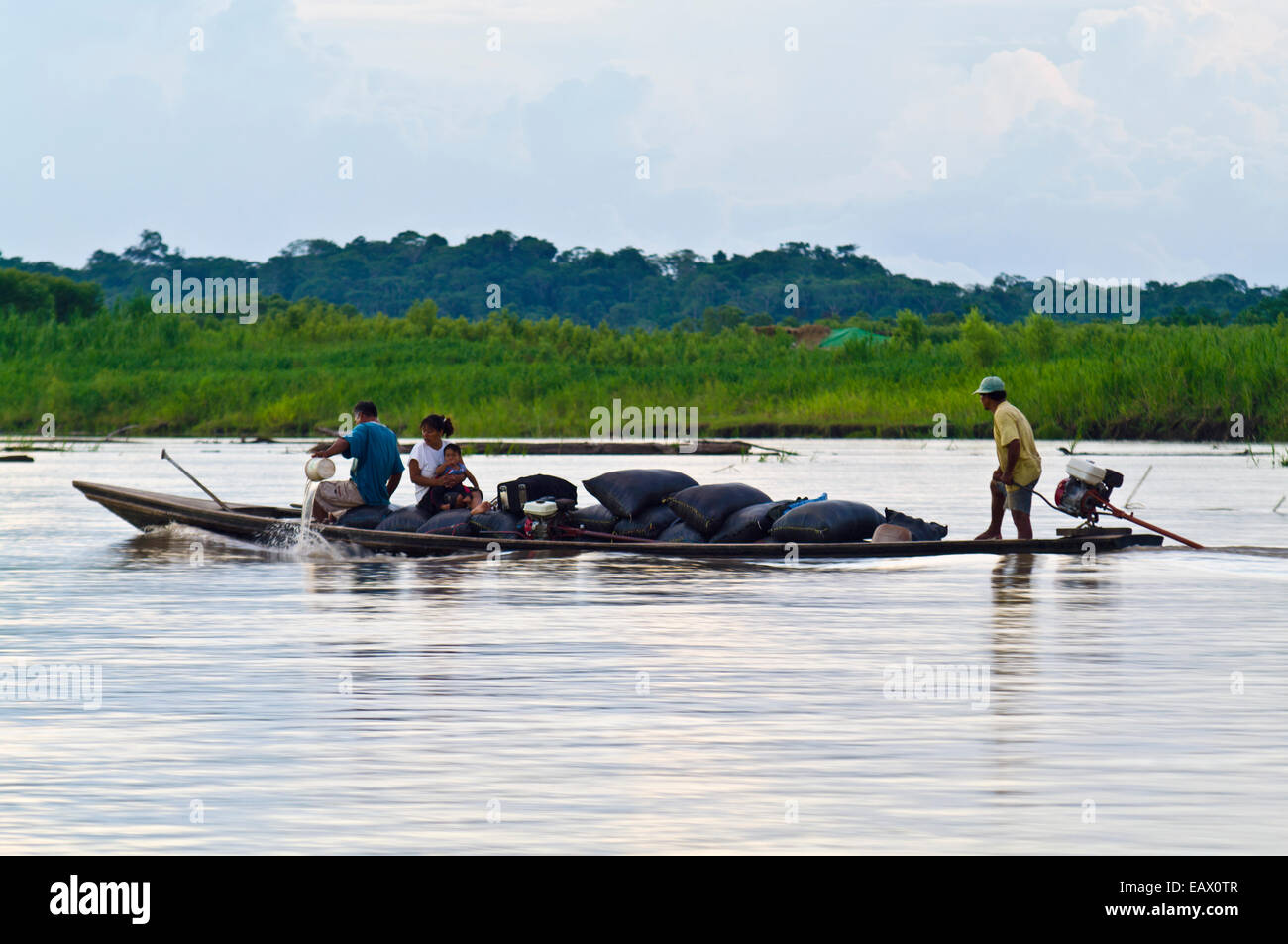 A villager bails water from a heavily laden water taxi carrying goods and a family to market. Stock Photo