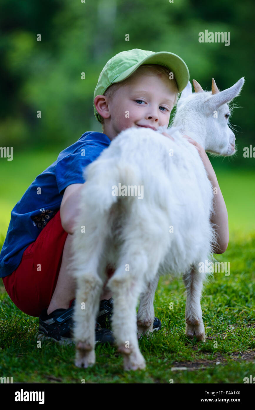 Young boy hugs a white goat on a farm Stock Photo