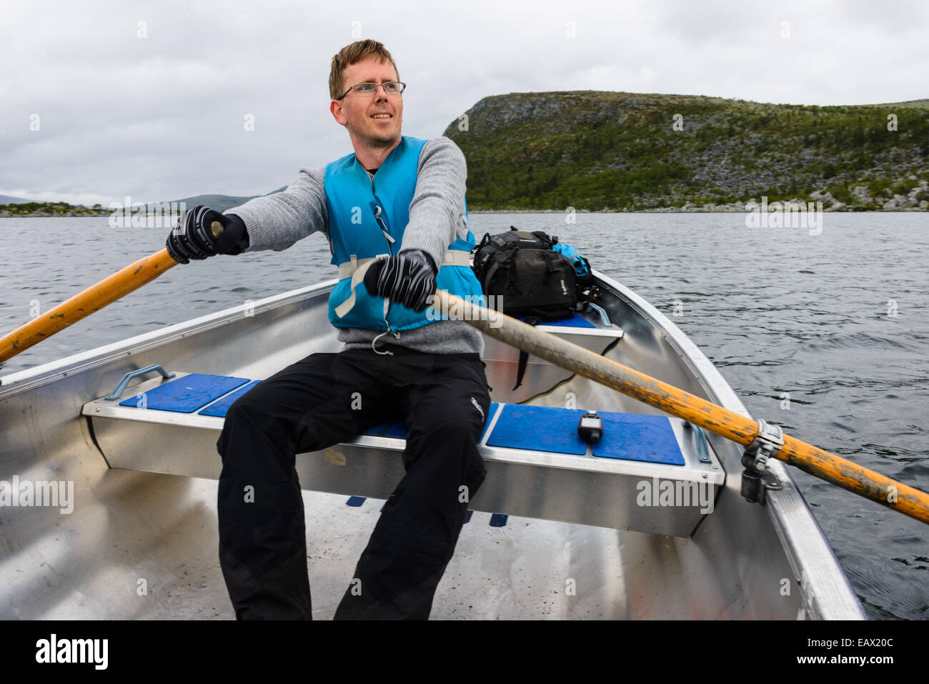 Rower in a blue life jacket rowing on a lake Stock Photo