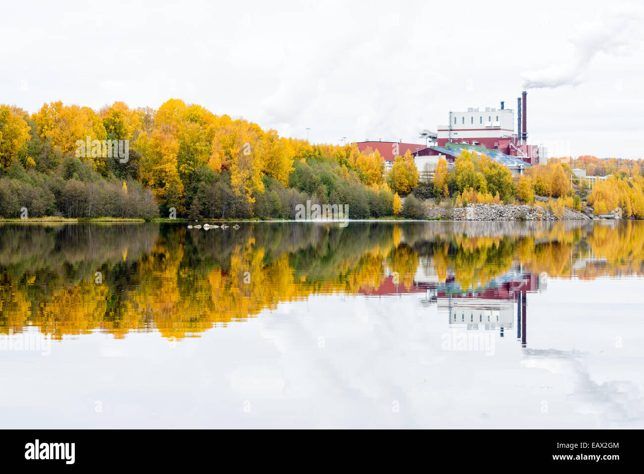 Factory with a smokestack reflected on a still lake Stock Photo