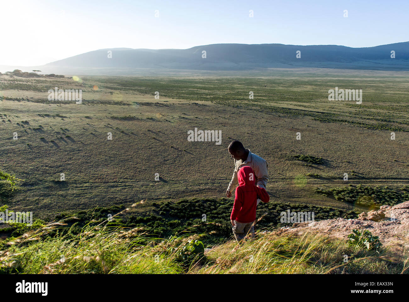 A safari guide assists a small child to climb down the steep surface of a rocky outcrop. Stock Photo
