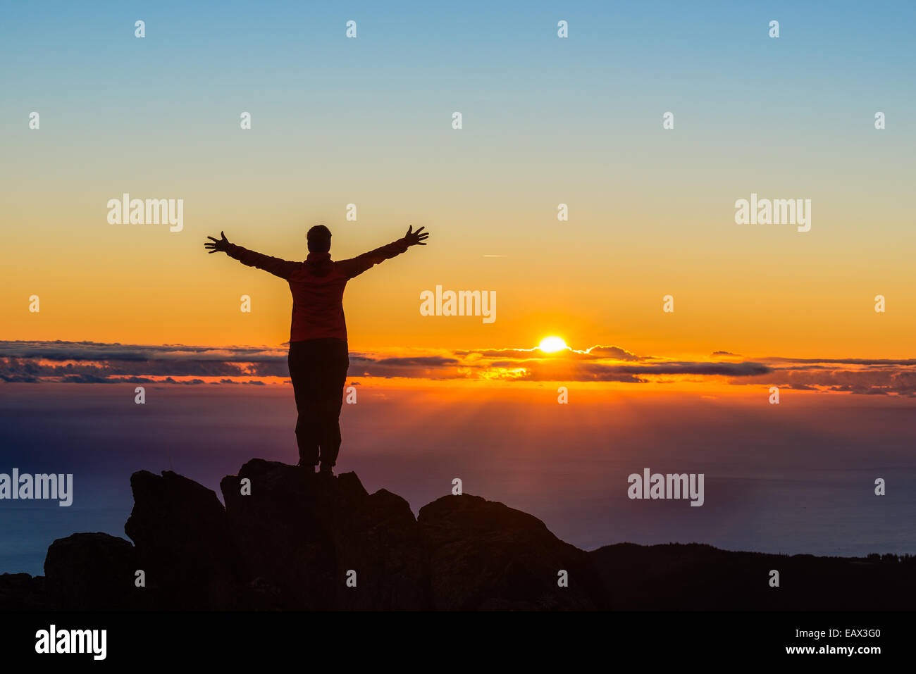 Hiker with arms raised atop a mountain at sunrise Stock Photo