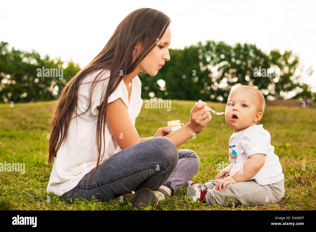 Young beautiful mother feeding her baby puree outdoors in sunlight