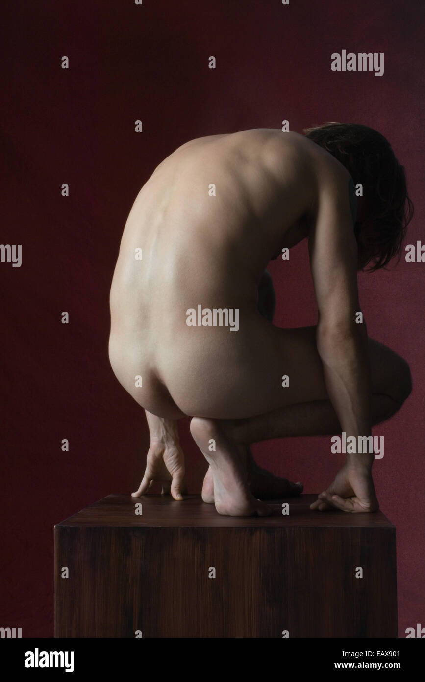 Nude man crouching on pedestal Stock Photo