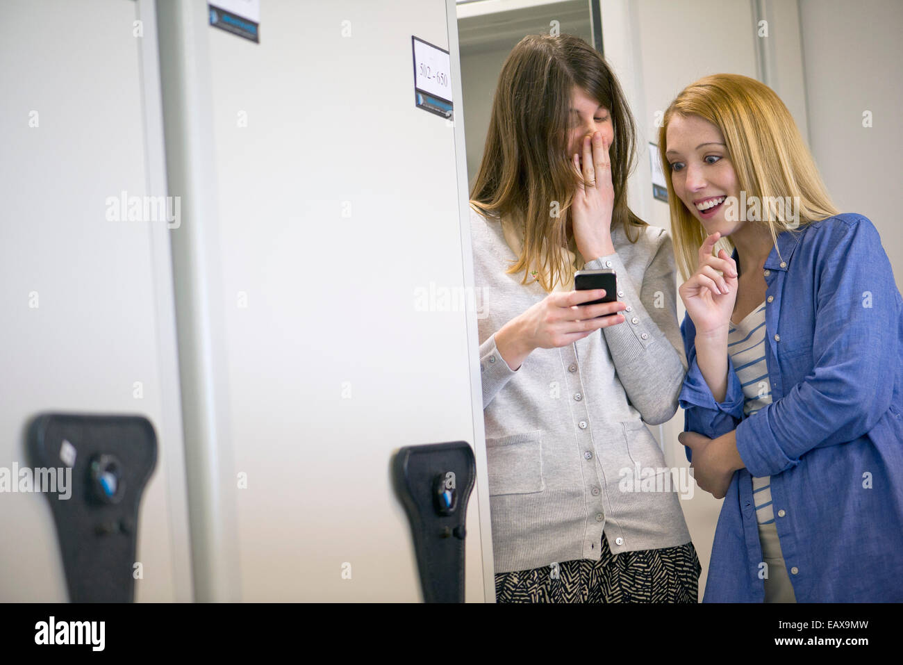 Women laughing at smartphone in office Stock Photo
