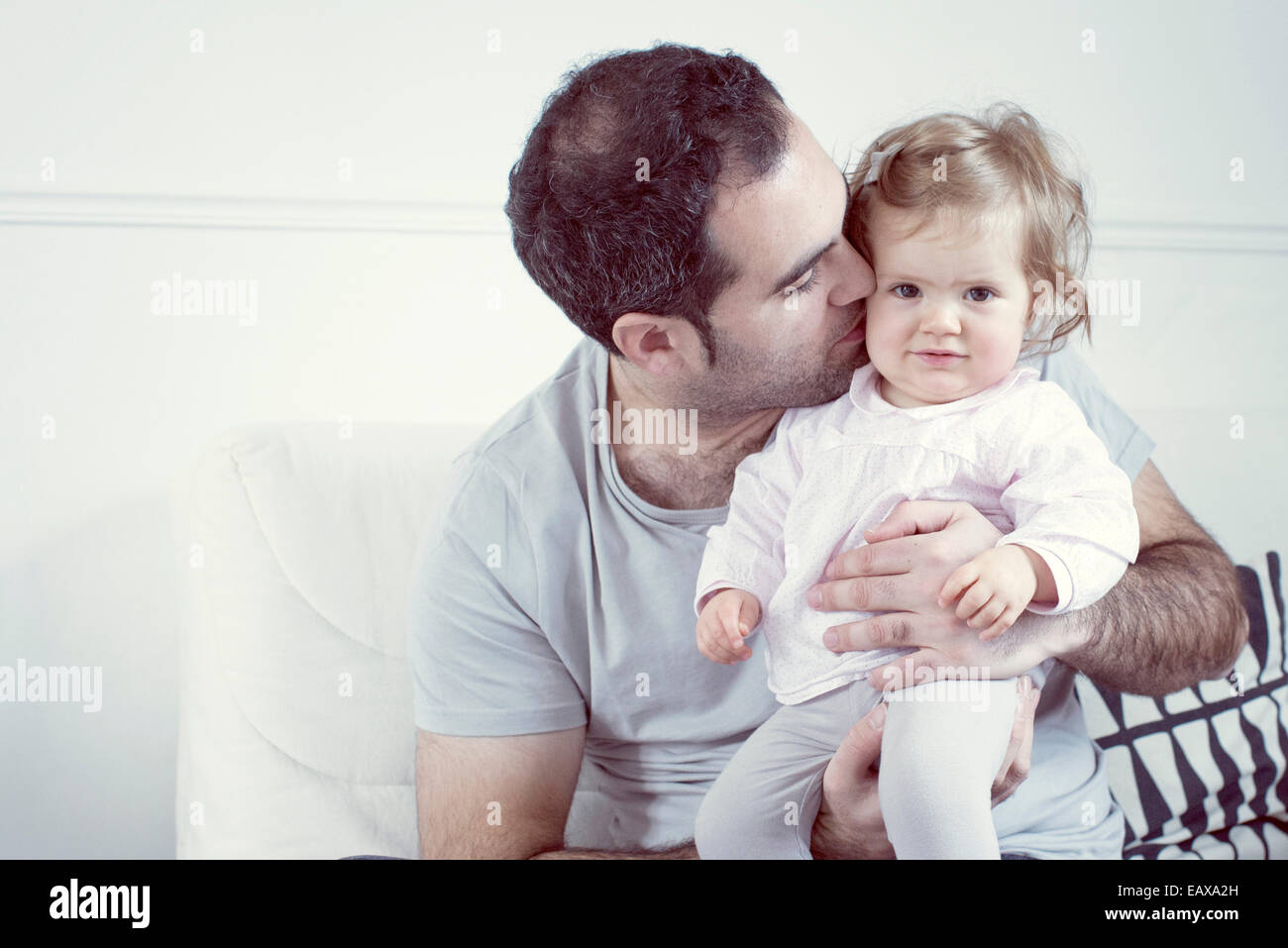 Father holding baby girl on lap, kissing her cheek Stock Photo