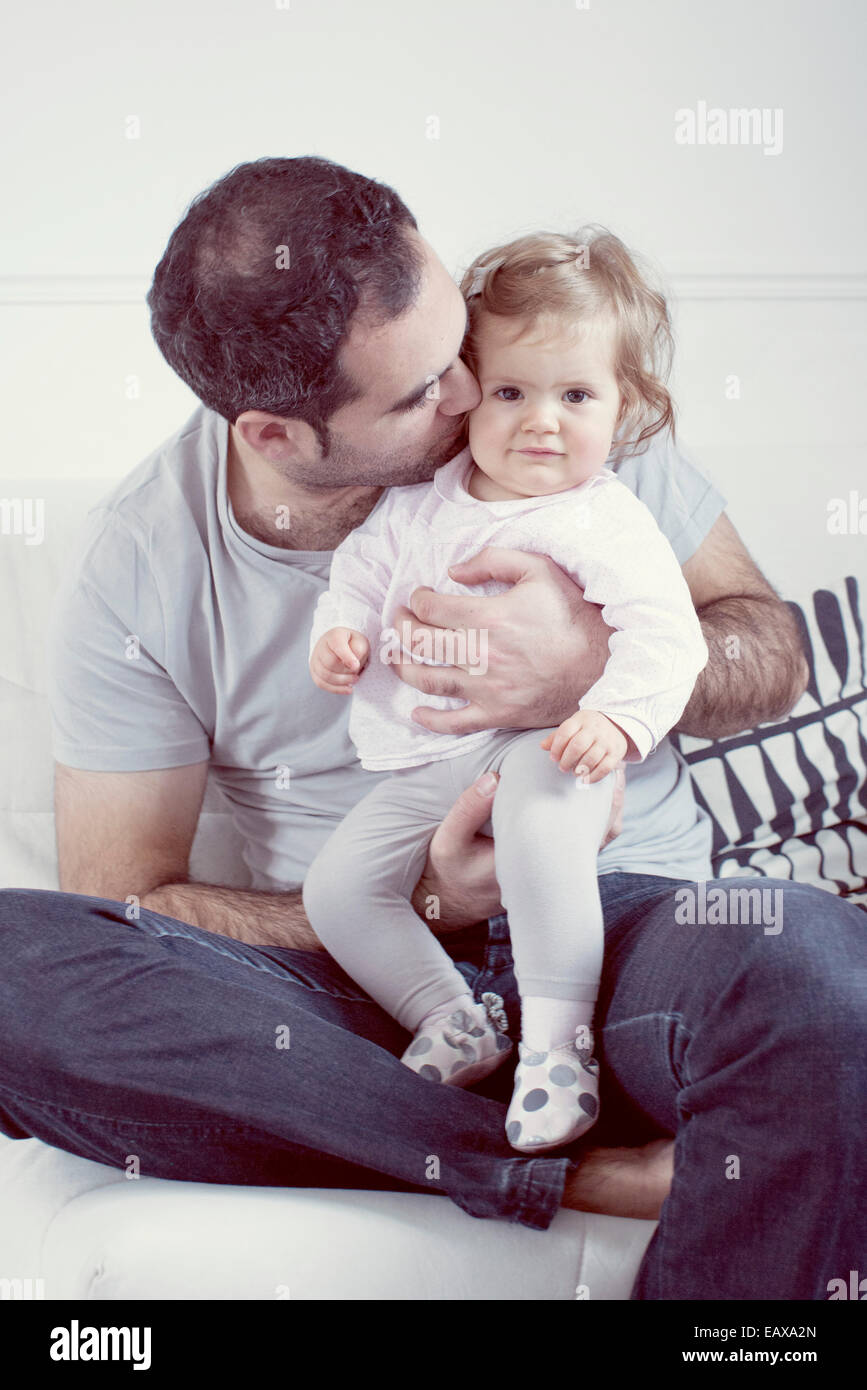 Father holding baby girl on lap, kissing her cheek Stock Photo