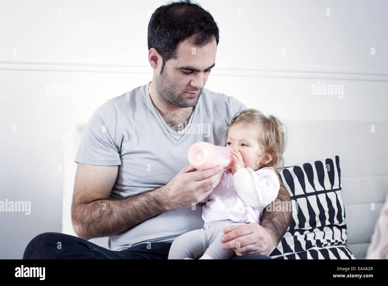 Father holding baby girl on lap, feeding her with bottle Stock Photo
