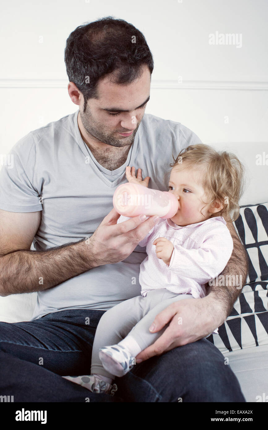 Father holding baby girl on lap, feeding her with bottle Stock Photo