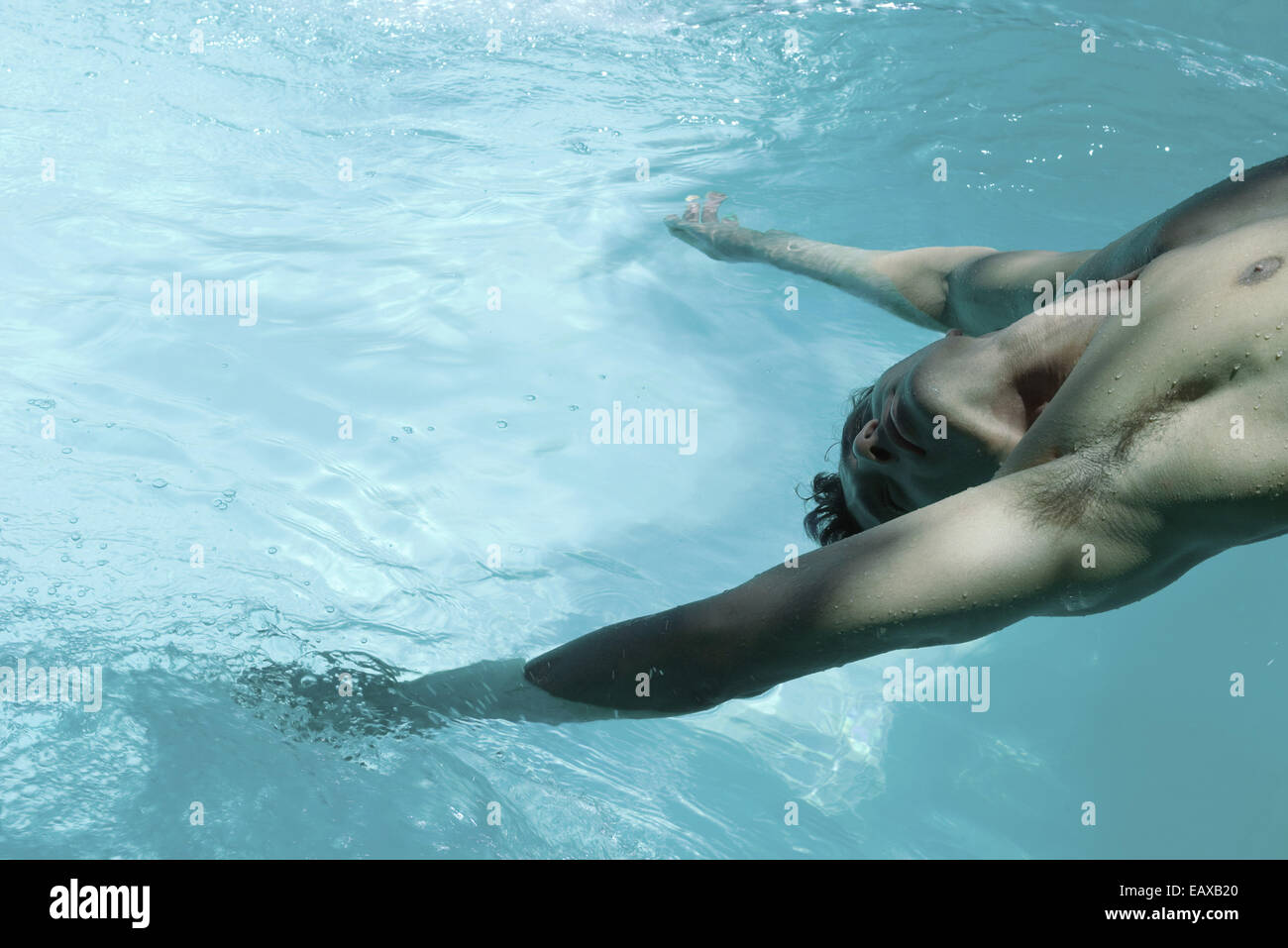 Man leaning backward over swimming pool, dangling arms in water Stock Photo