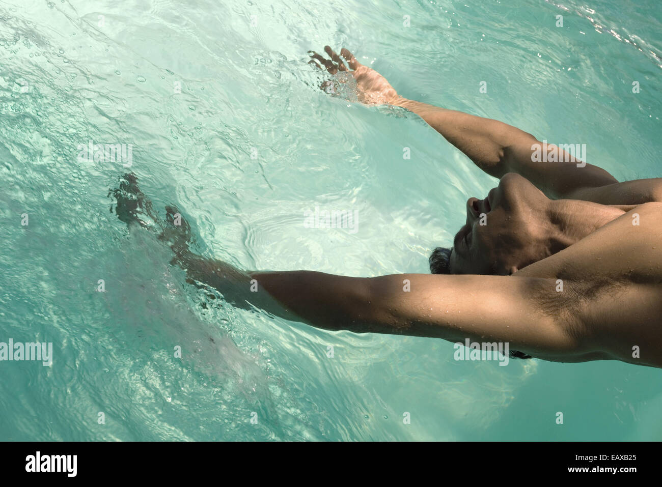 Man leaning backward over pool, arms in water Stock Photo
