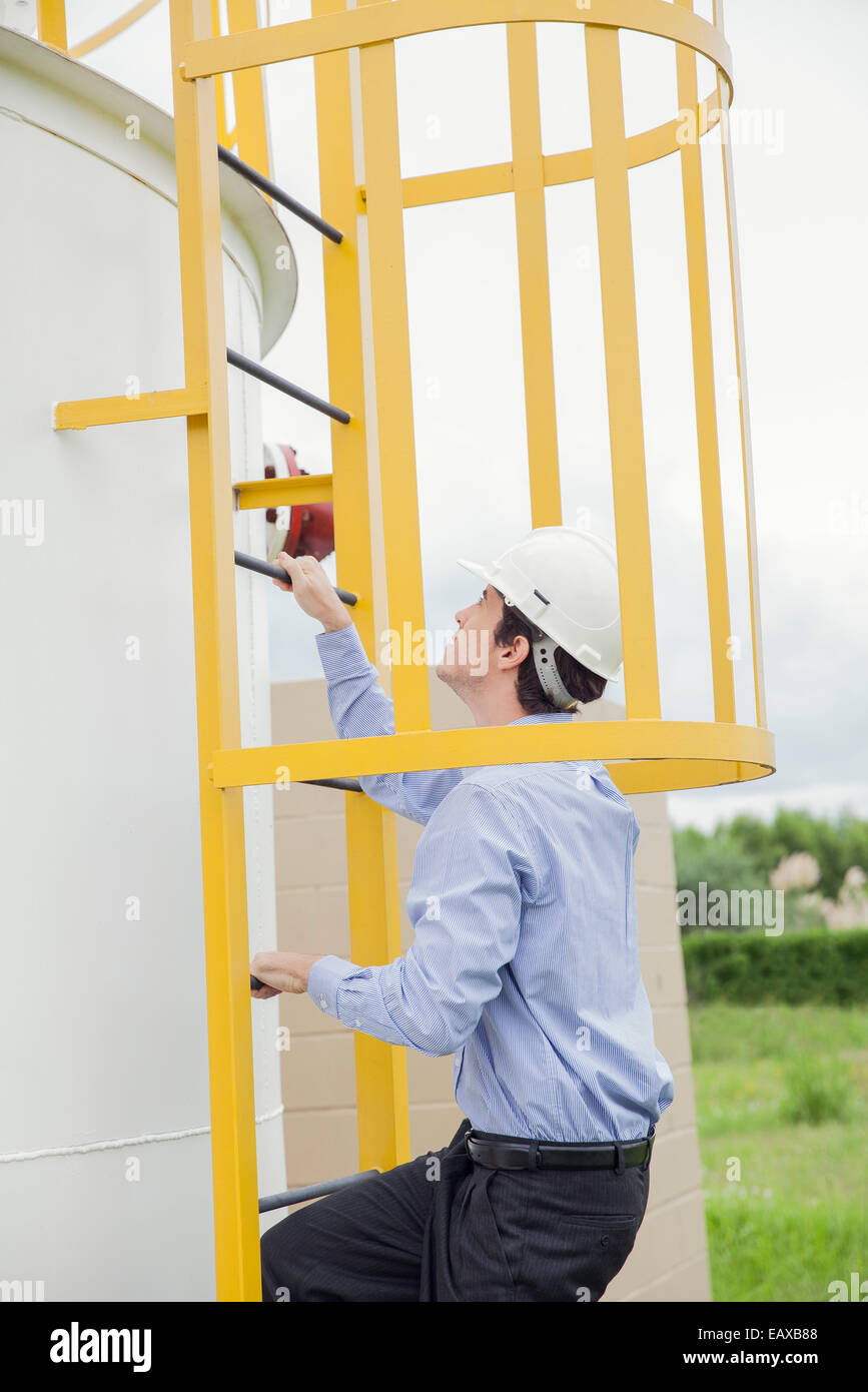 Engineer climbing storage tank ladder at industrial site Stock Photo
