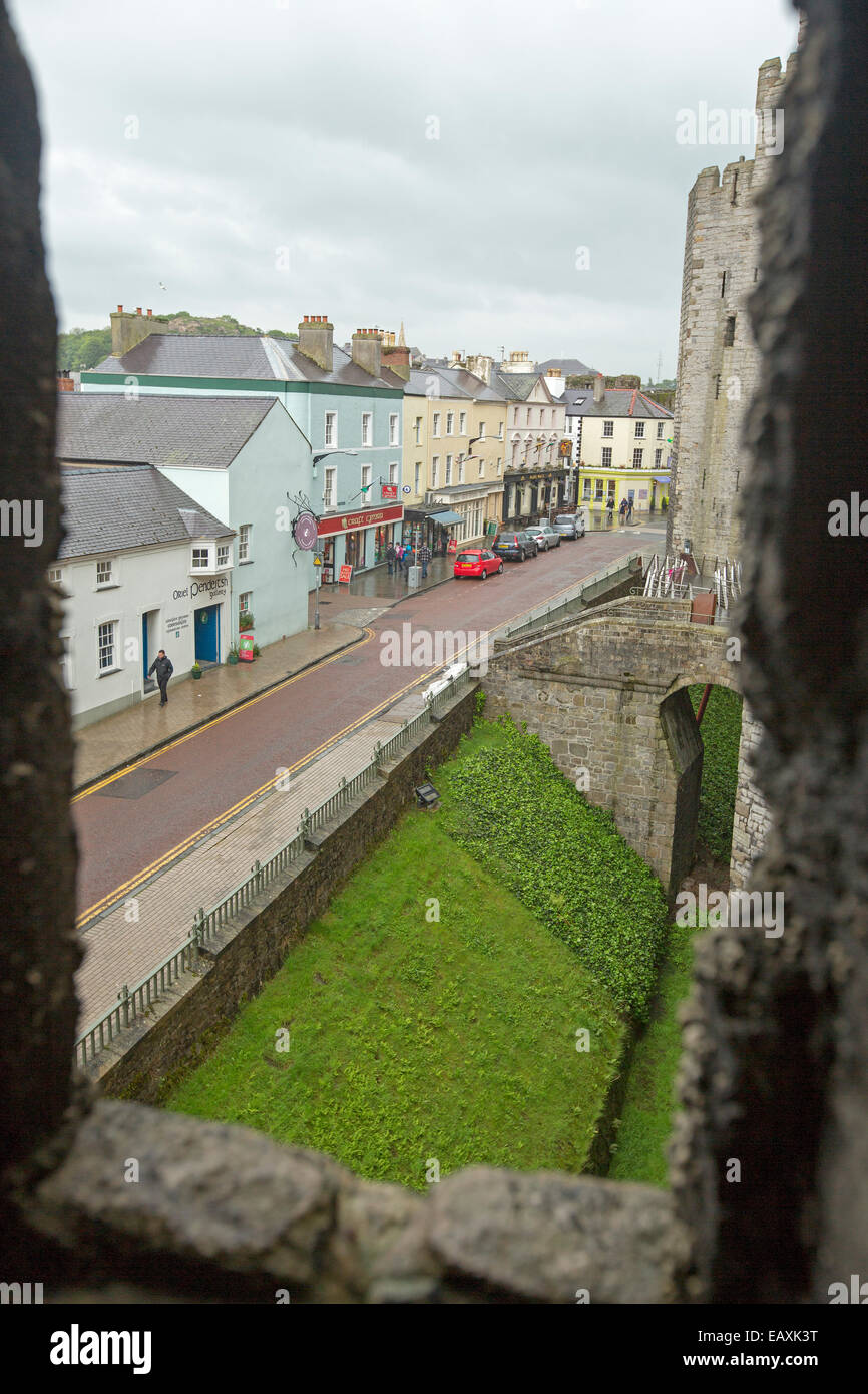 View of ancient stone wall of castle, narrow street with row of colourful shops & houses from high window of Caernarfon castle Stock Photo