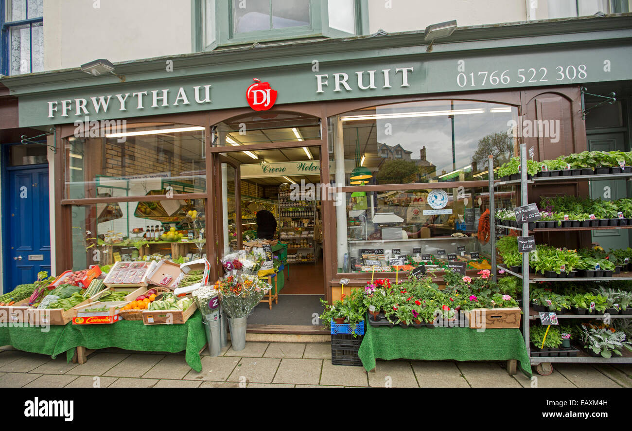 Fruit shop in Criccieth, Wales with signs in both English & Welsh, boxes of fruit on sale on footpath stall & customer inside Stock Photo