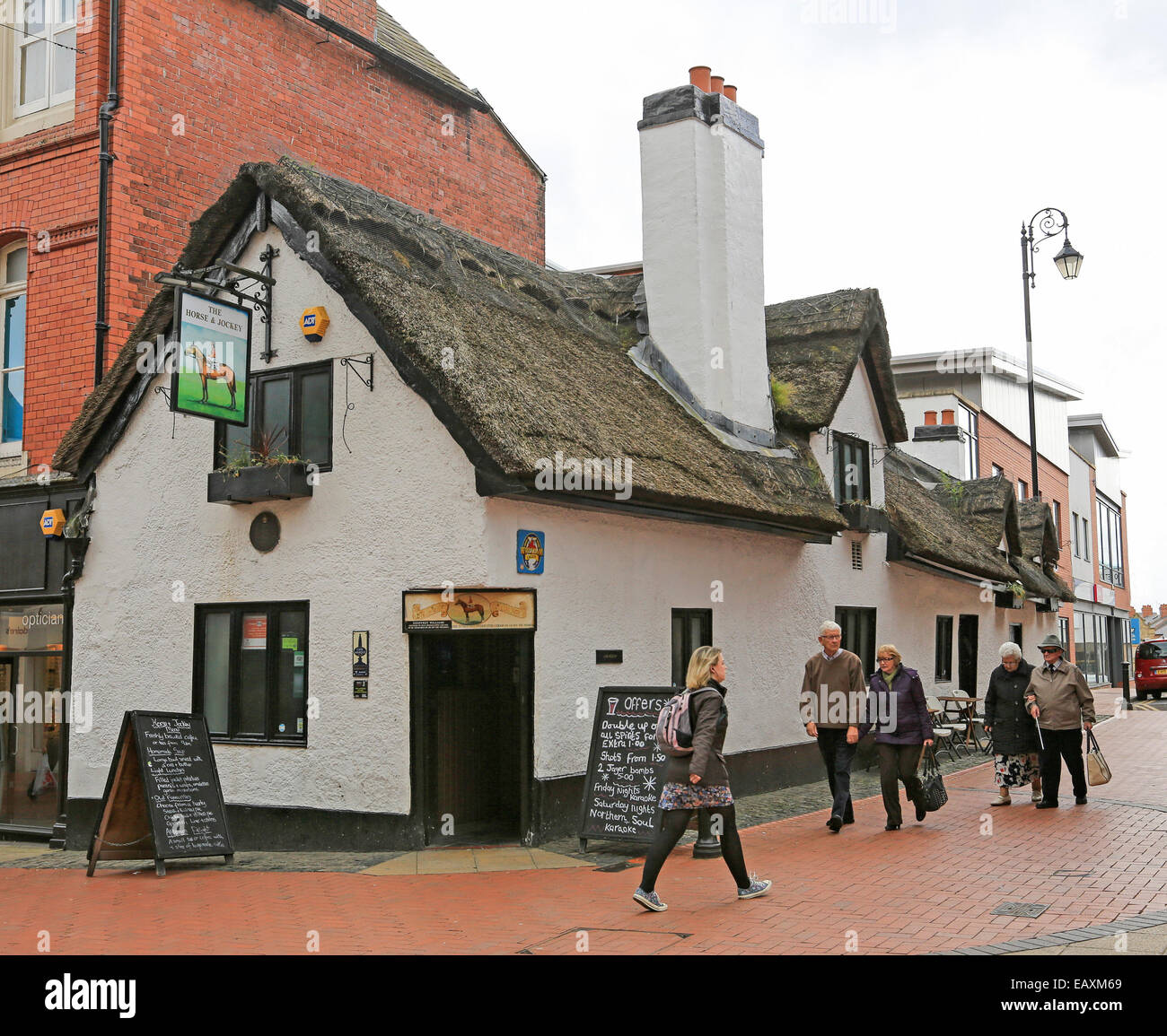 Historic 17th century Horse and Jockey pub with white painted walls & thatched roof with people walking past - in Wrexham, Wales Stock Photo