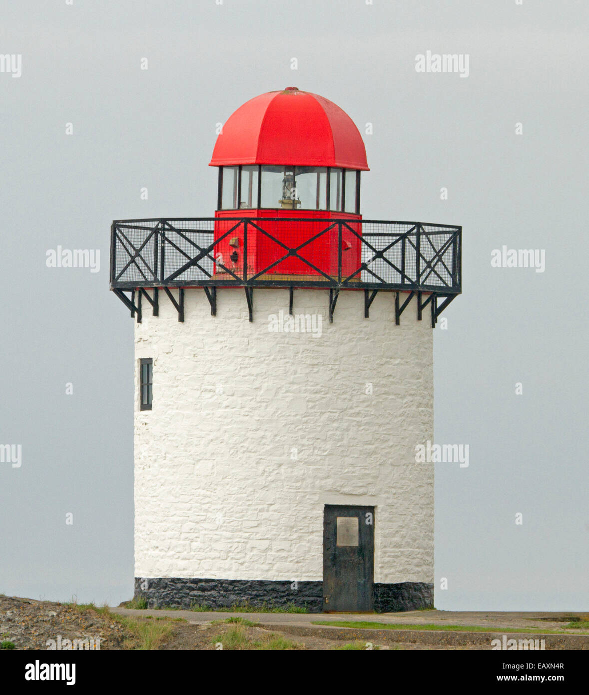 Old restored & operational lighthouse with white cylindrical tower and bright red domed light at Burry Port harbour in Wales Stock Photo