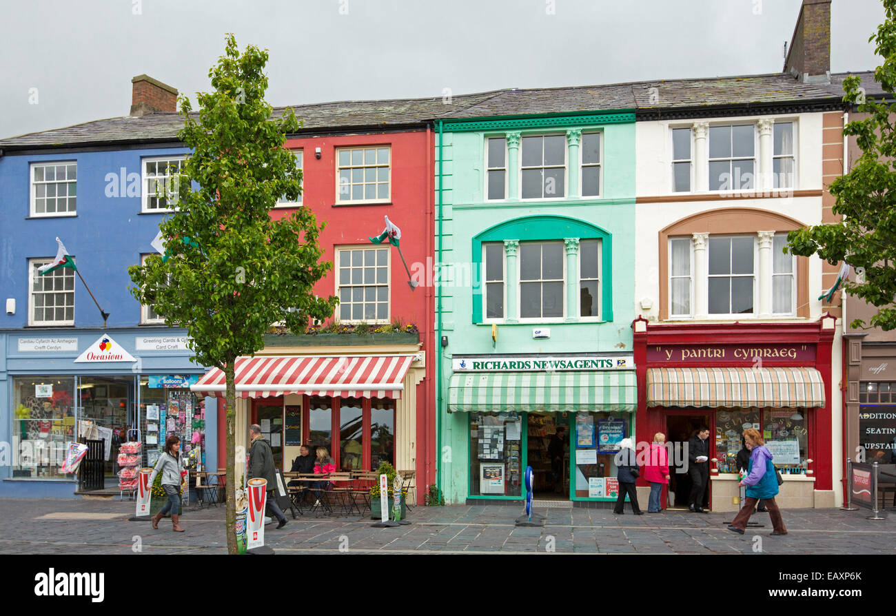 Row of brightly painted shops with striped awnings & shoppers wandering past in Castle Square / The Maes at Caernarfon, Wales Stock Photo