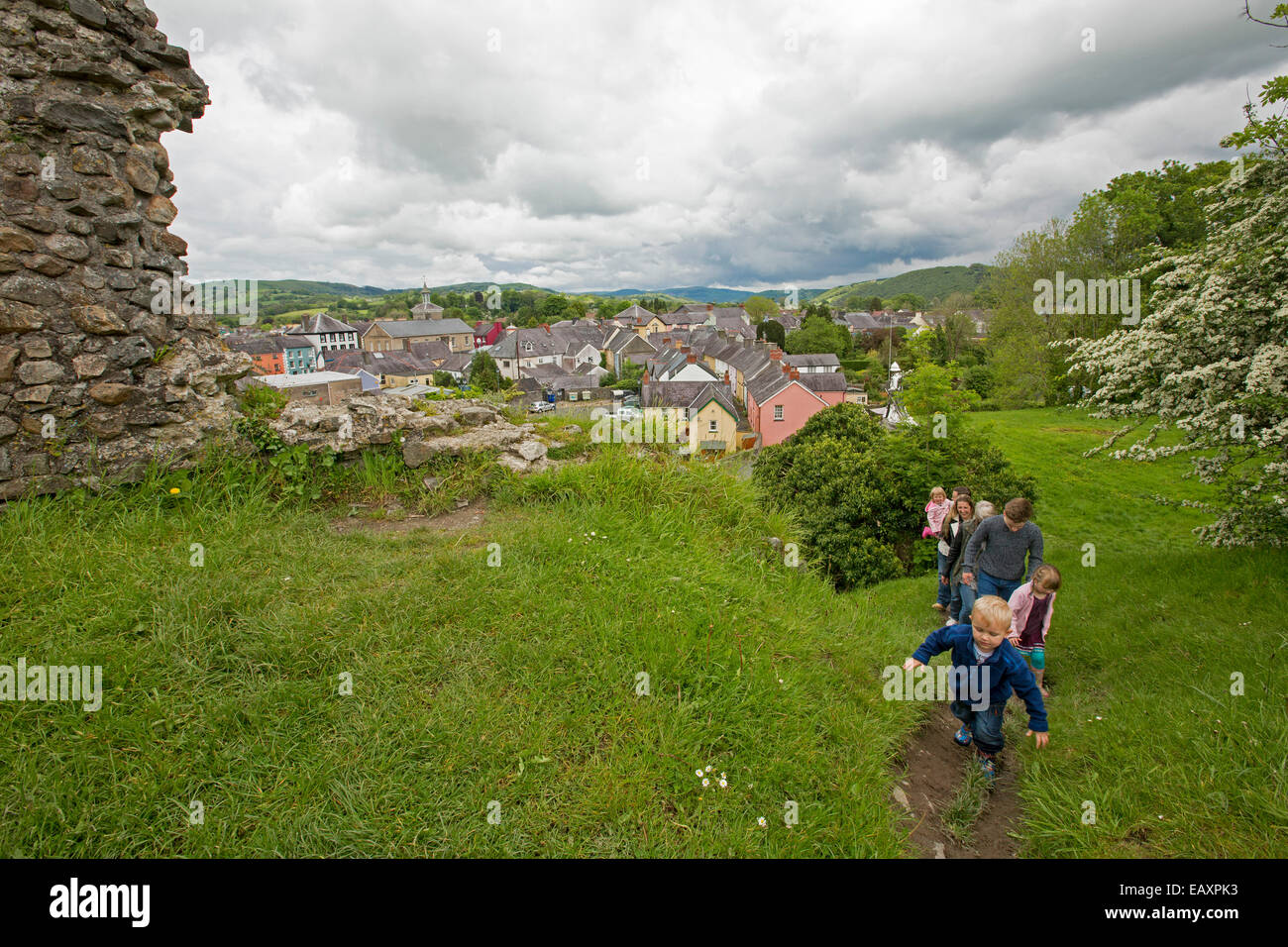 View of Welsh town of Llandovery from hilltop ruins of castle with family walking to summit on narrow track through grass Stock Photo
