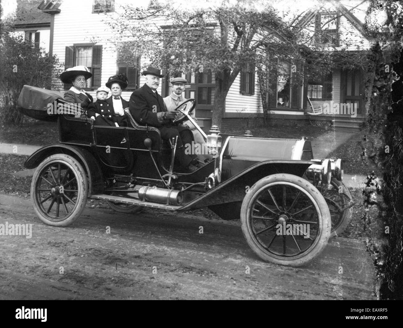 Family in old car in front of house Stock Photo