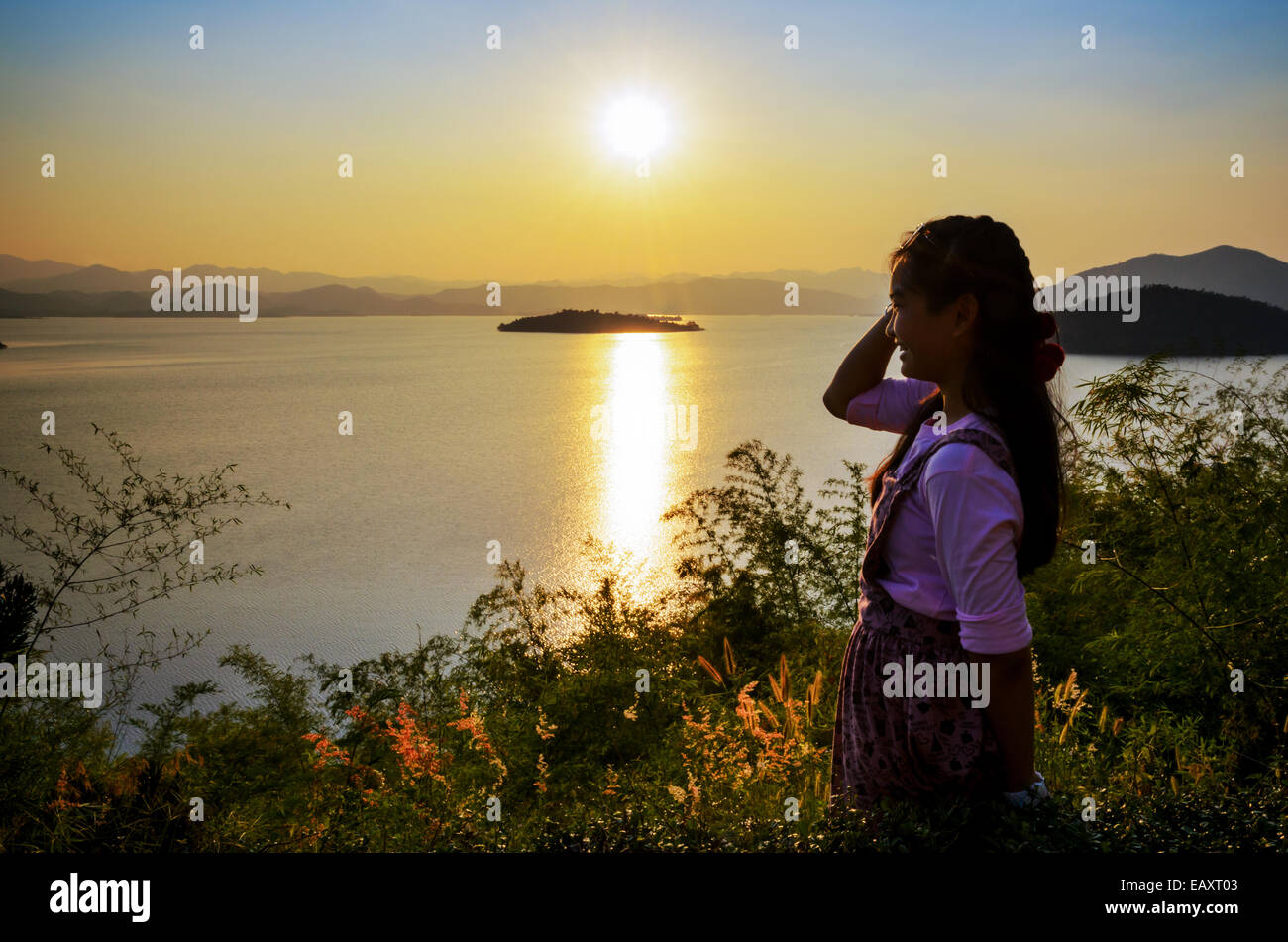 Happy young woman standing on the hill watching the sunset over the lake in Kaeng Kra Chan National Park, Phetchaburi Province,  Stock Photo