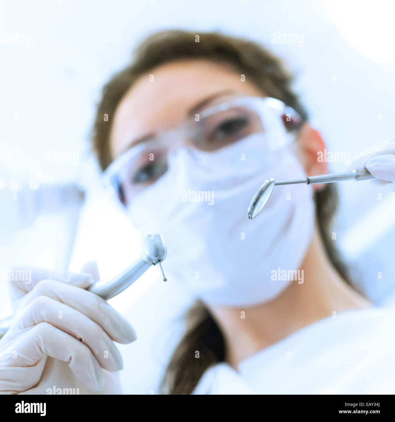 Dentist wearing surgical mask while holding angled mirror and drill