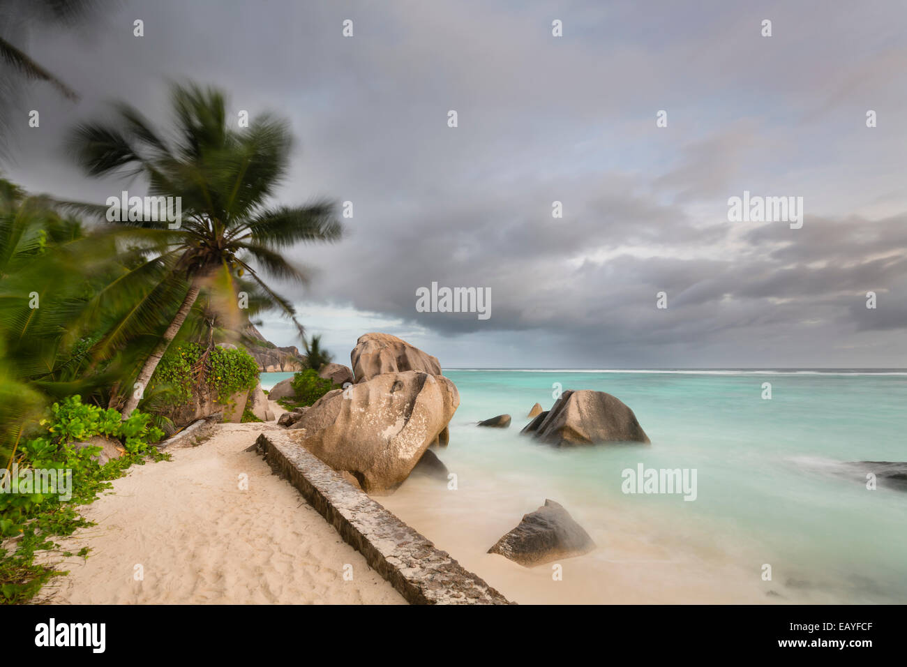 Dark clouds over the beach Anse Source D'Argent in La Digue, Seychelles with scenic granite rocks and palm trees Stock Photo