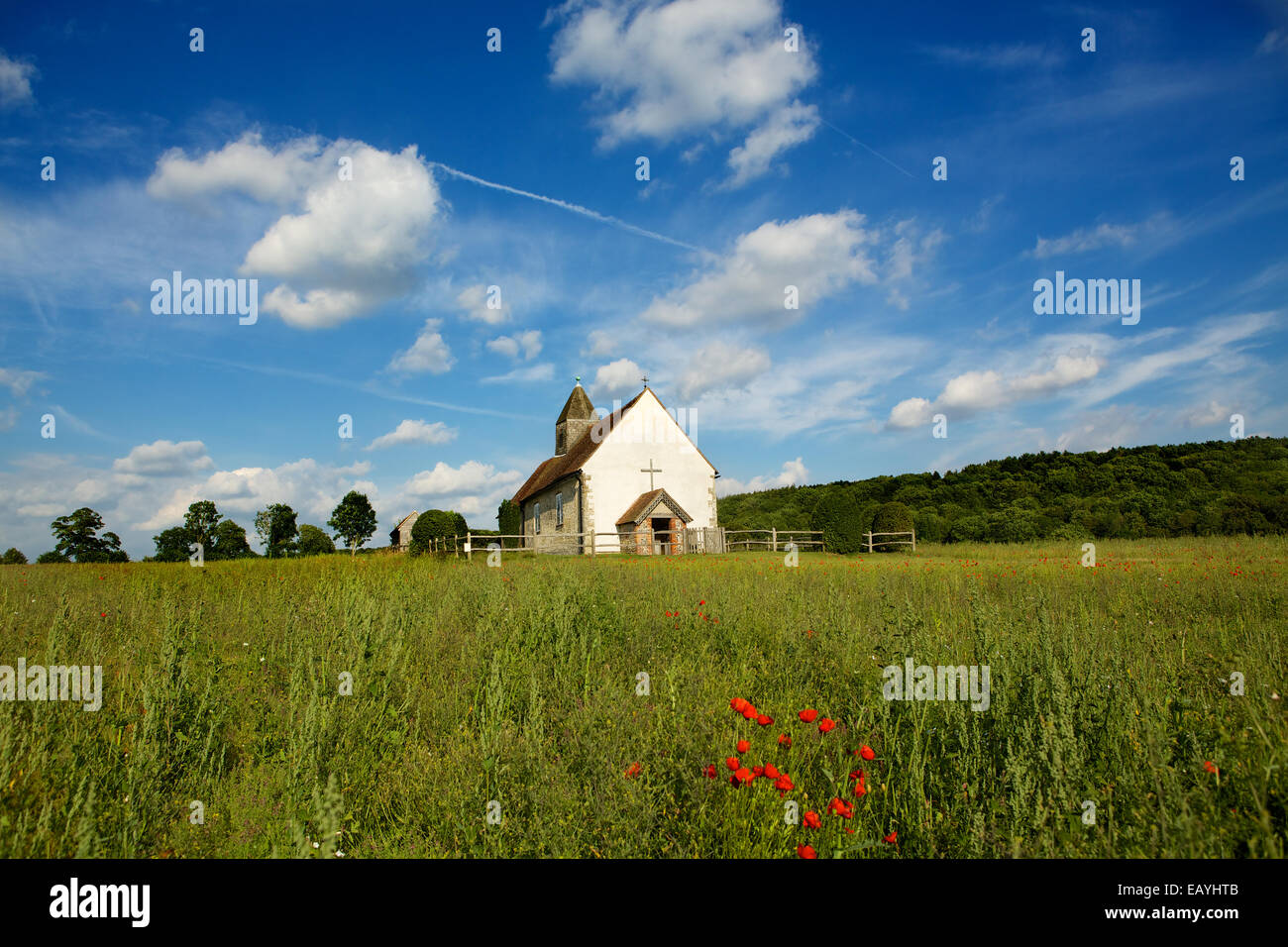 Church on the Hill. St Hubert's  a small medieval church standing alone in a wild meadow. Red poppies in the foreground. Stock Photo