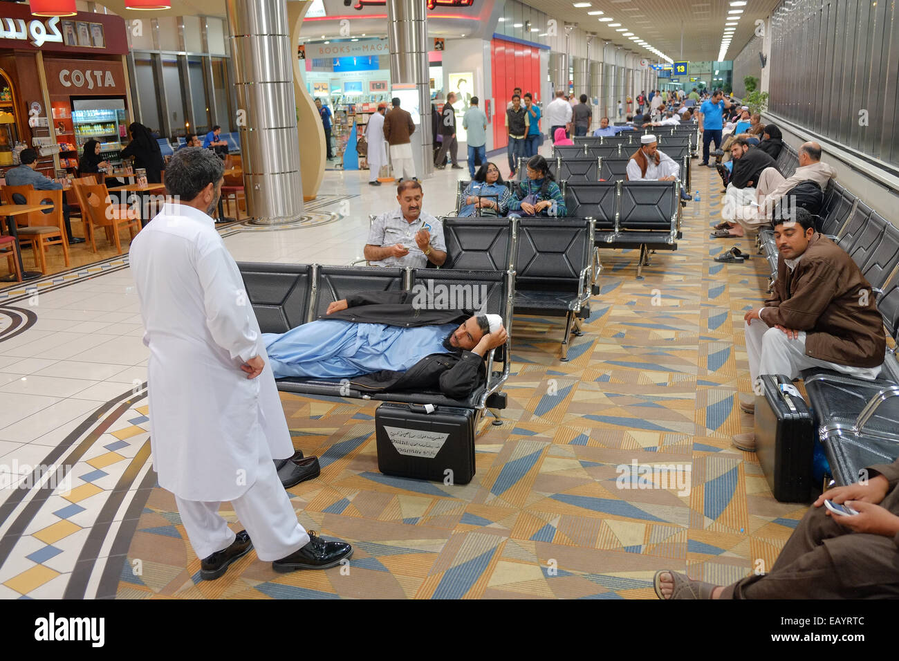 Getting some rest prior to boarding their flight at the departure lounge at Bahrain International Airport, Bahrain, Middle East. Bahrain has a population of over 55% immigrants and was a general election on this day. Stock Photo