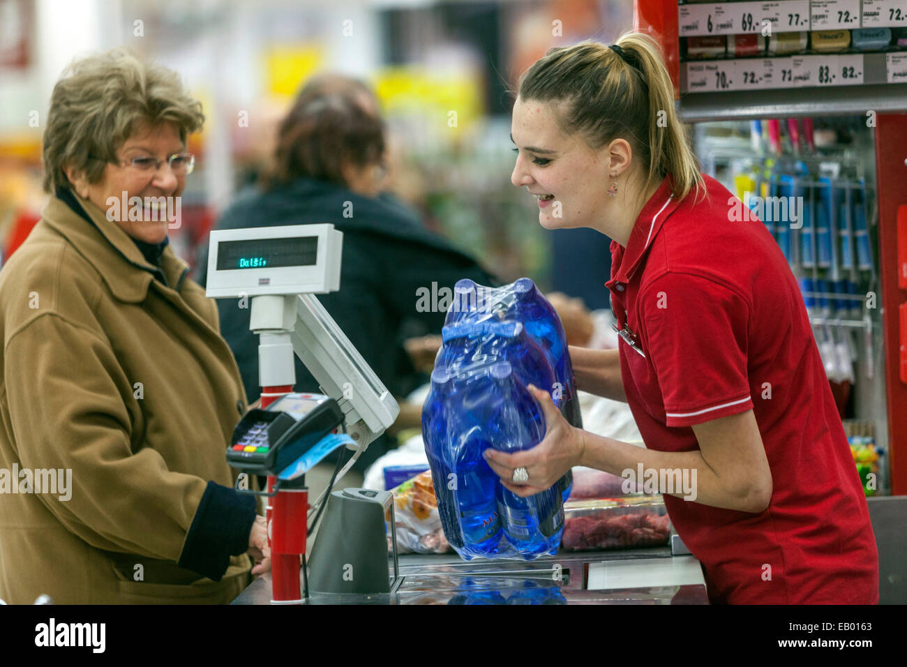 People Senior woman shopping in supermarket checkout Cashier woman reads barcodes of water bottles Stock Photo