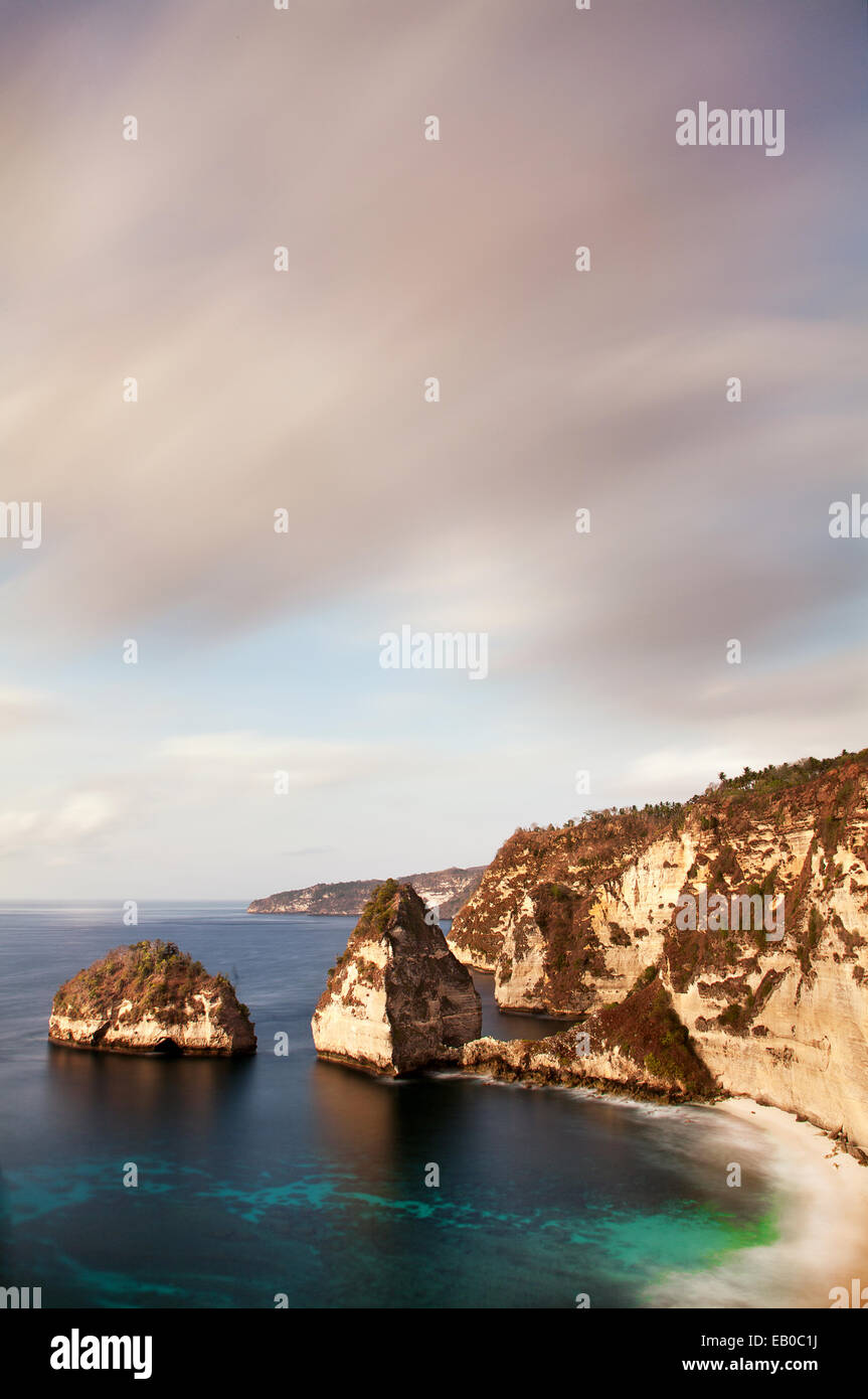 Long exposure image of incredible Karst scenery landscape on Nusa Penida Island at sunset with dramatic sky and unique shaped sea stacks in the sea Stock Photo